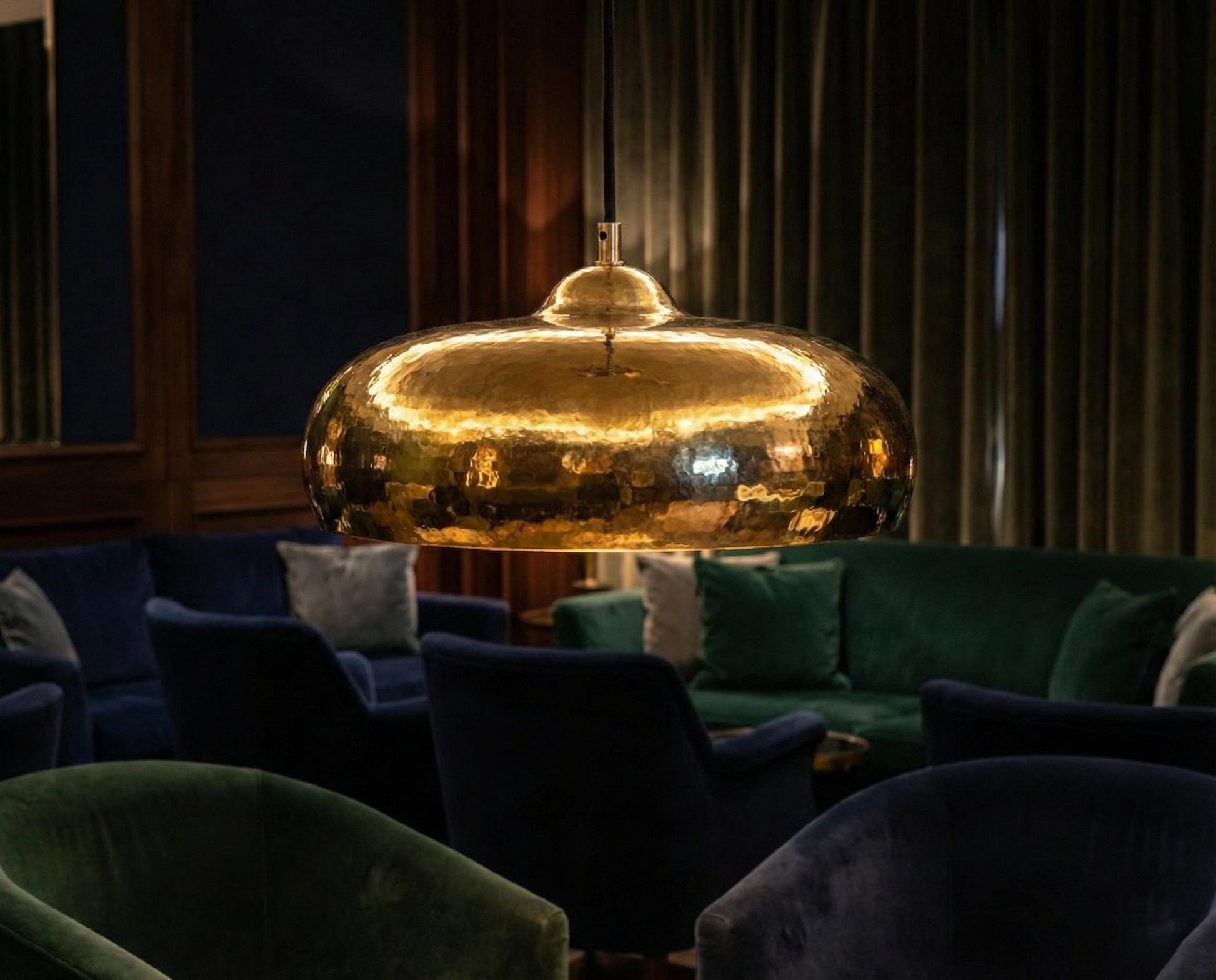 Large golden pendant light in a dimly lit room with green sofas and cushions.