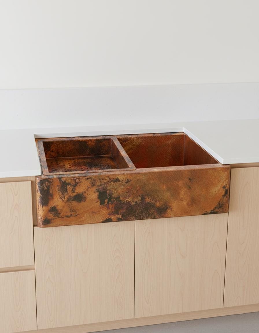 Copper kitchen sink embedded in wooden cabinetry with a white wall background