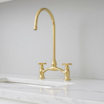Gold kitchen faucet on a marble countertop with a white wall background