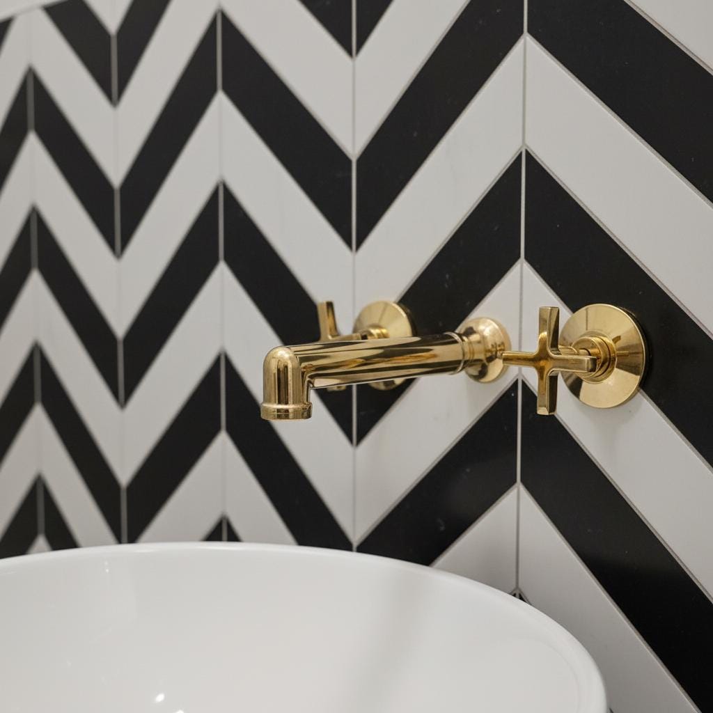 Gold faucet on a white sink with black and white chevron patterned wall tiles.