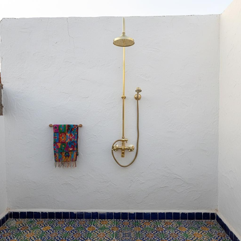 Shower setup with gold fixtures on a white wall with blue tiled base.