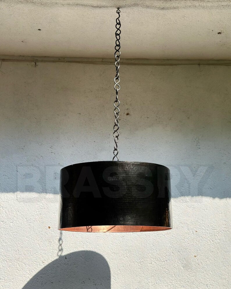 Handcrafted Moroccan black copper drum pendant light hanging over a dining table

