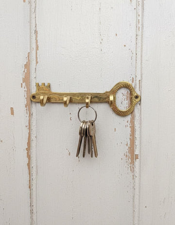 Decorative brass key hook with keys on a white wooden background