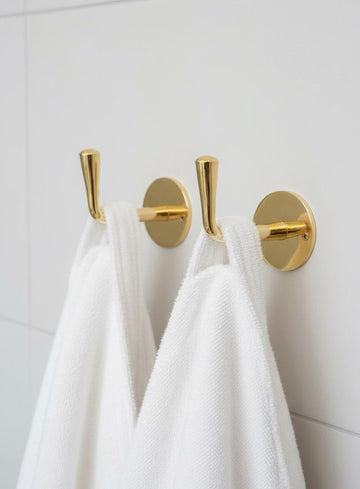 Gold towel hooks on a white wall with white towels hanging from them.