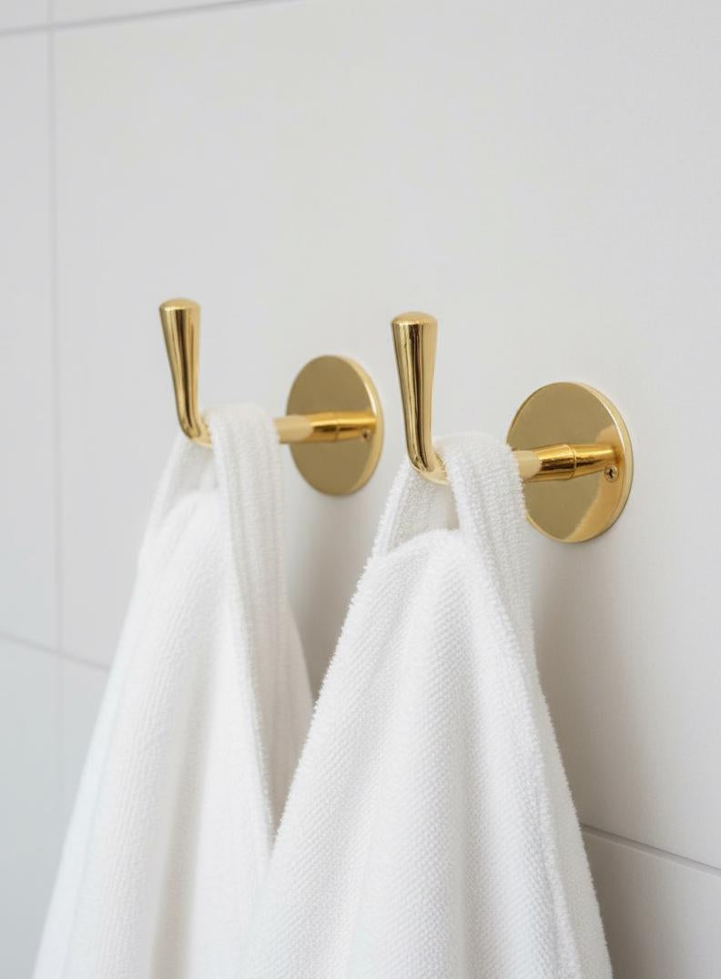 Gold towel hooks on a white wall with white towels hanging from them.