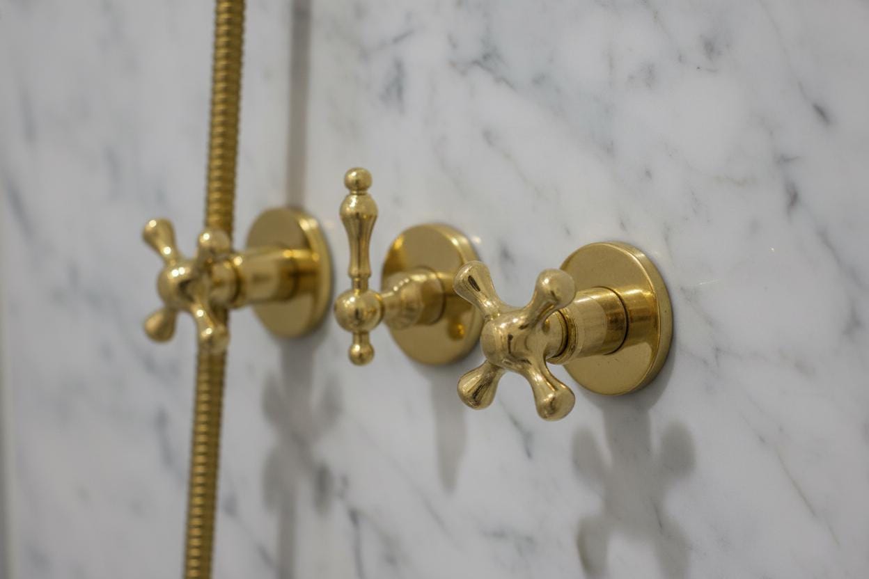 Gold bathroom faucet and shower head on a marble wall