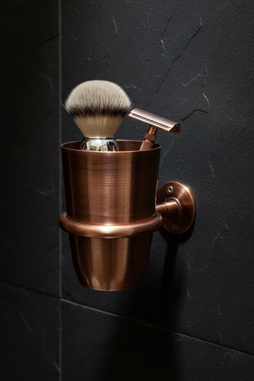 Bronze shaving brush and stand against a dark tiled wall