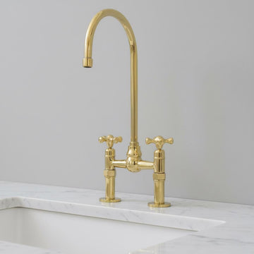 Gold kitchen faucet on a marble countertop with a light gray wall background