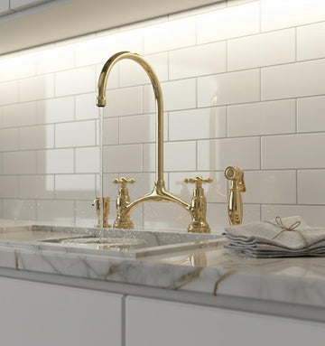 Gold kitchen faucet and handles on a marble countertop with white tiled wall.