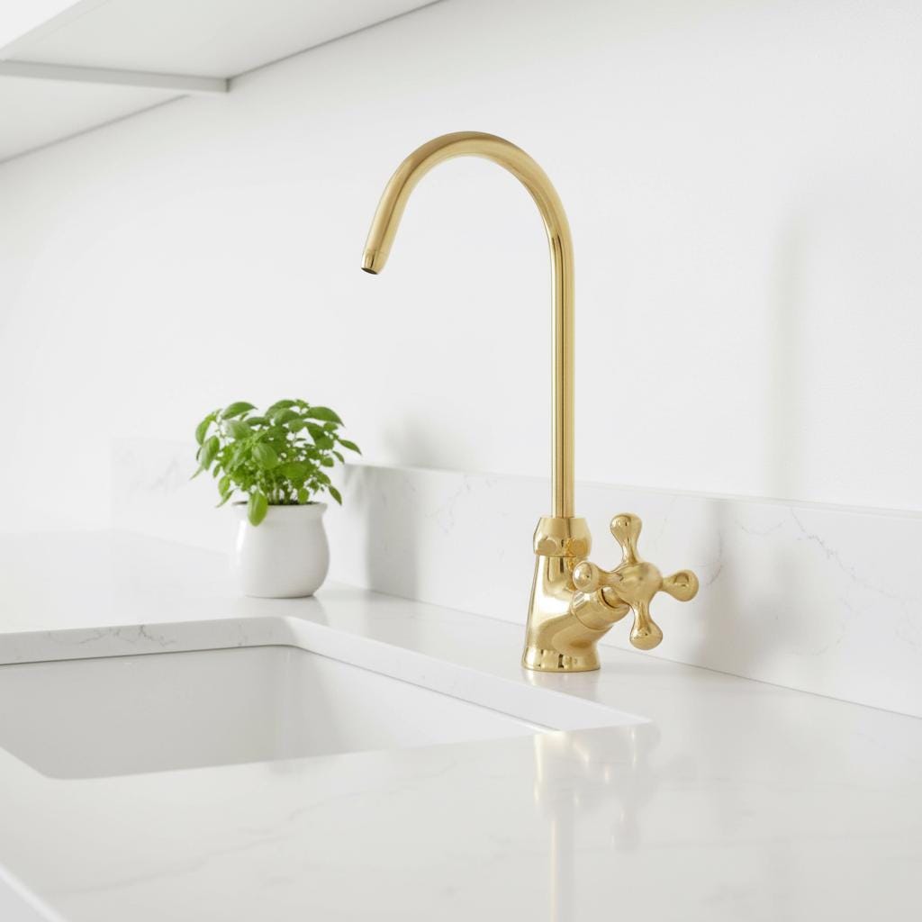 Gold kitchen faucet on a white countertop with a small plant in the background