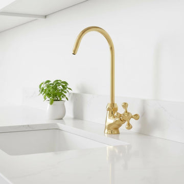 Gold kitchen faucet on a white countertop with a small plant in the background