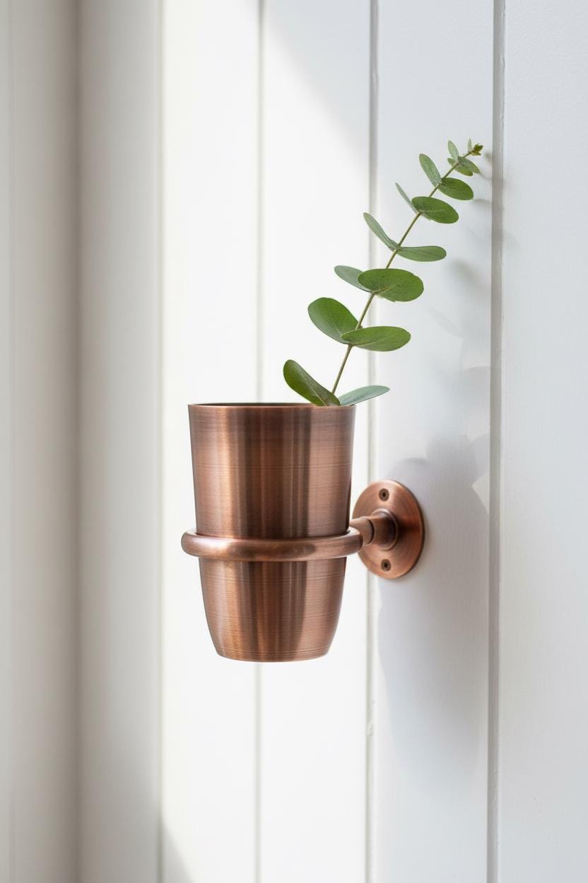 Copper wall-mounted plant holder with a plant against a white wall.