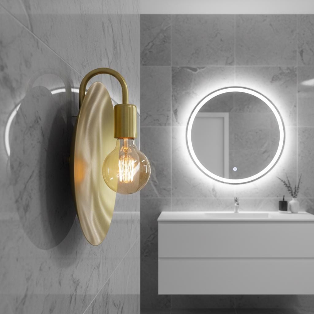Wall-mounted light fixture with a gold arm and beige shade on a white wall.
