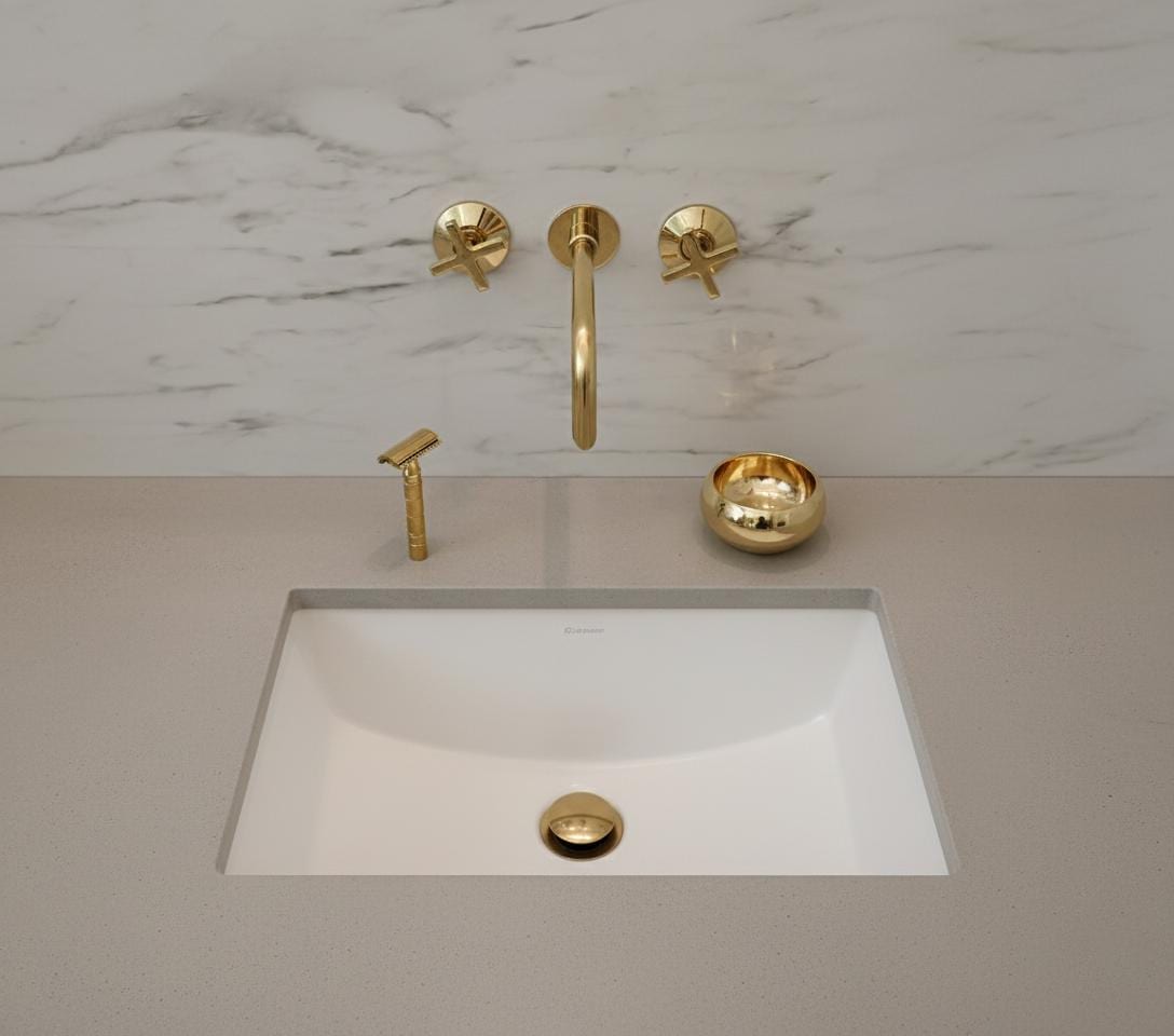 Gold bathroom faucet set on a marble wall with a white sink.