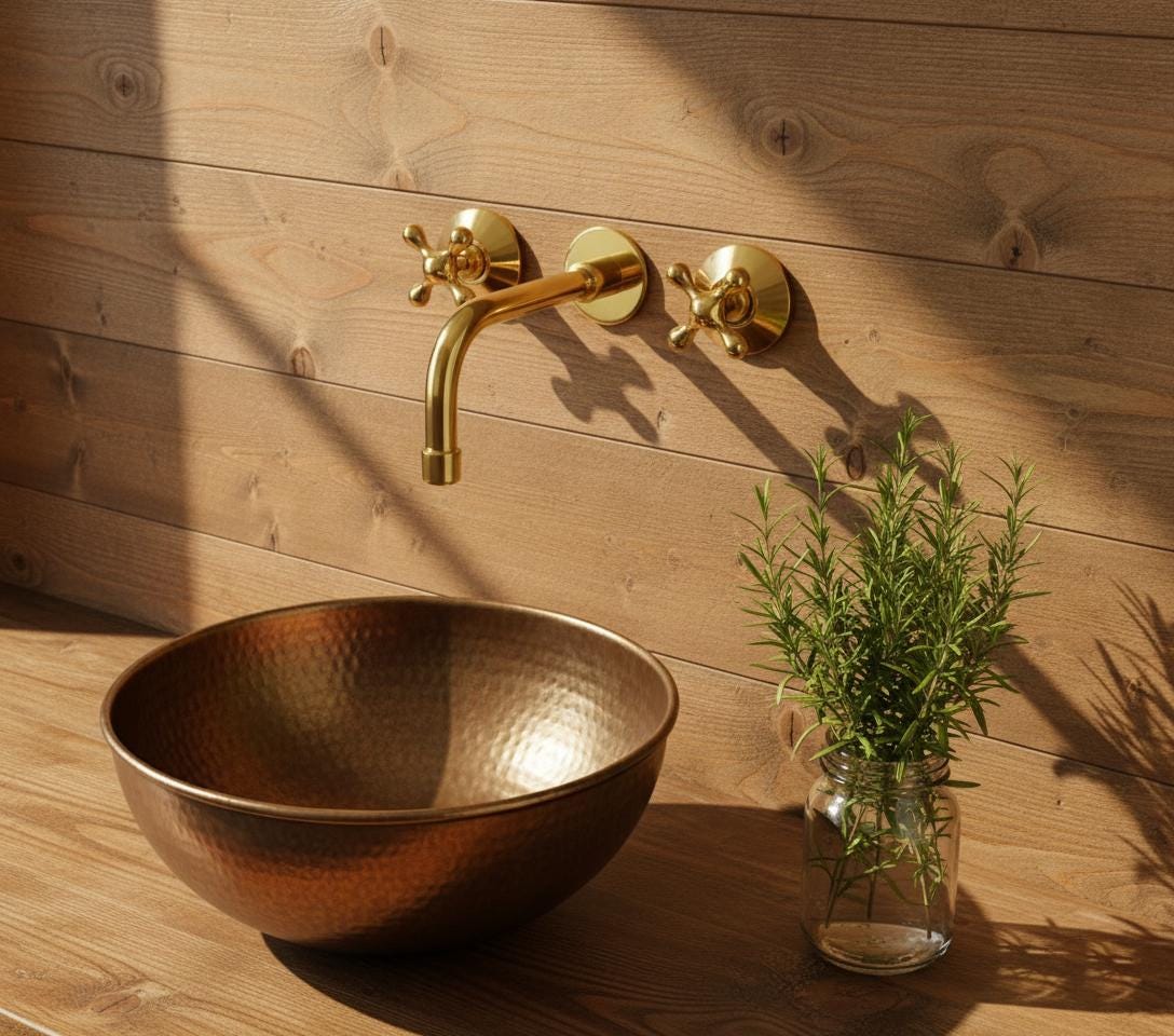Gold faucet and hammered bronze sink on a wooden wall with a plant in the foreground.