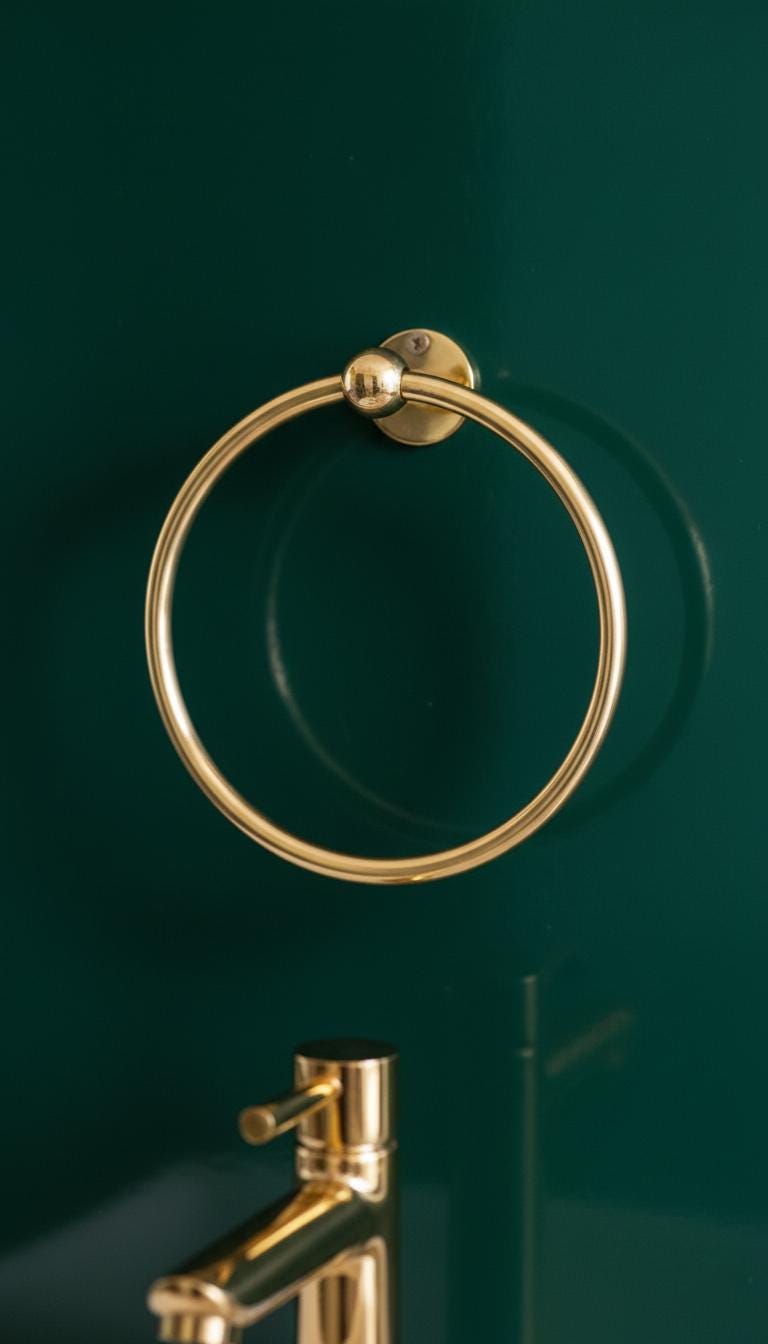 Gold towel ring on a white wooden wall with a beige towel and hand.