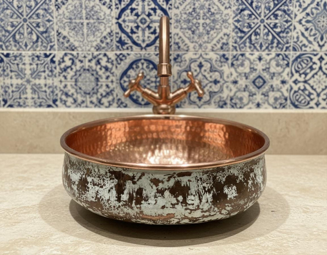 Copper sink on a marble countertop with floral wallpaper and a mirror above.
