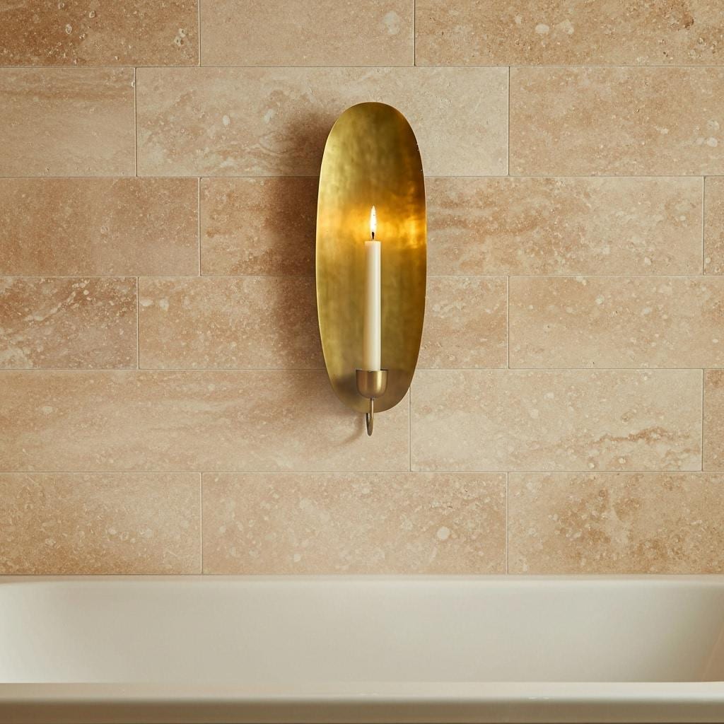 Brass wall sconce with a candle on a beige tiled wall.