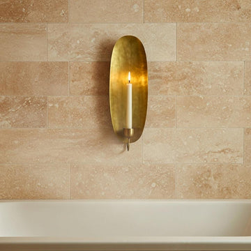 Brass wall sconce with a candle on a beige tiled wall.