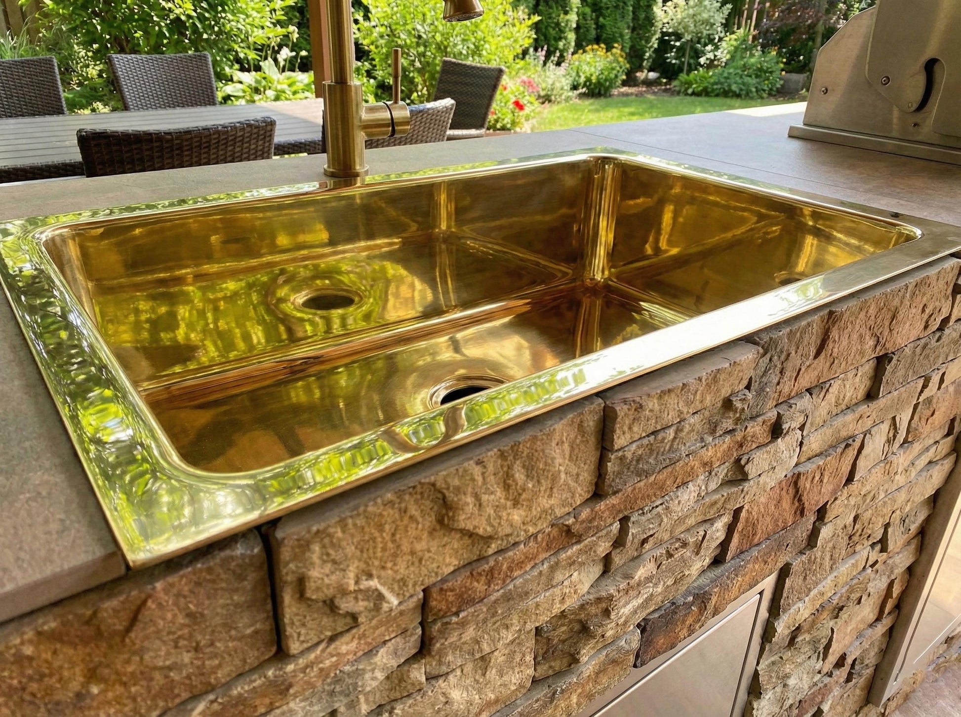Gold sink on a stone outdoor kitchen counter with garden view