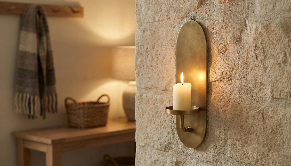 Brass wall sconce with a candle on a stone wall, with a cozy room setting in the background.