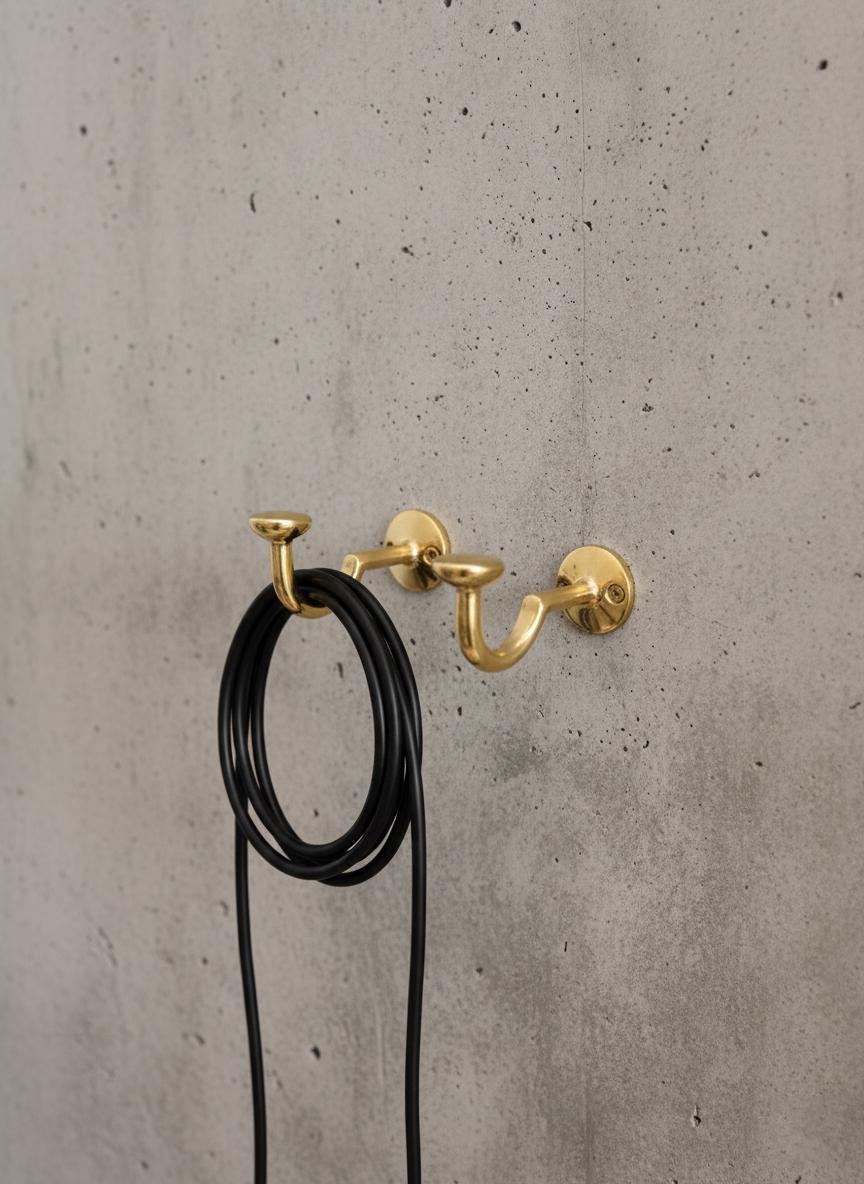 Gold wall hooks with black cord on a concrete wall