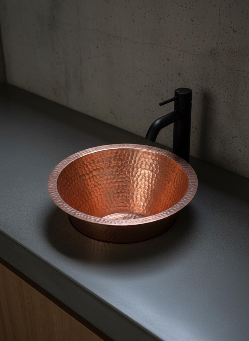 Copper sink on a gray countertop with a black faucet.