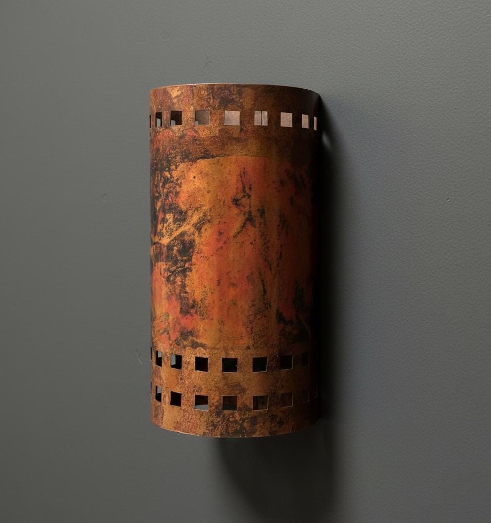 Rust-colored wall sconce with cut-out patterns on a gray wall