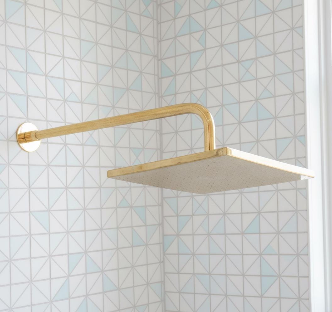 Gold shower head mounted on a tiled wall with geometric pattern
