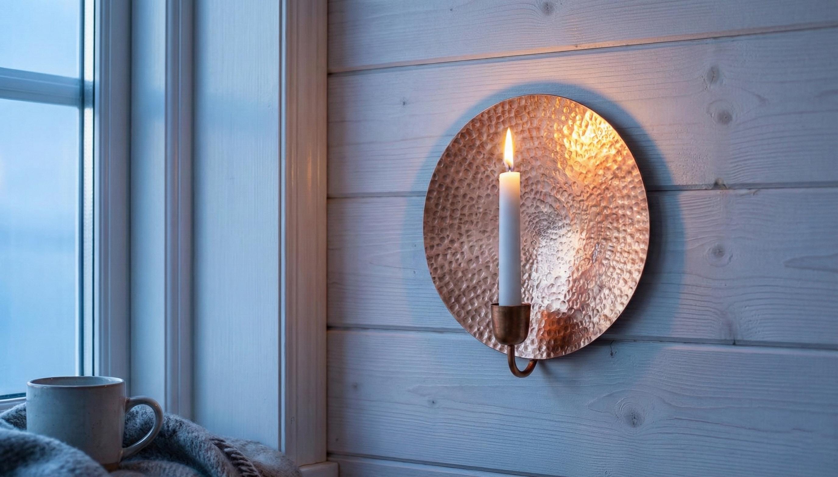 Copper wall sconce with a candle on a wooden wall next to a window.