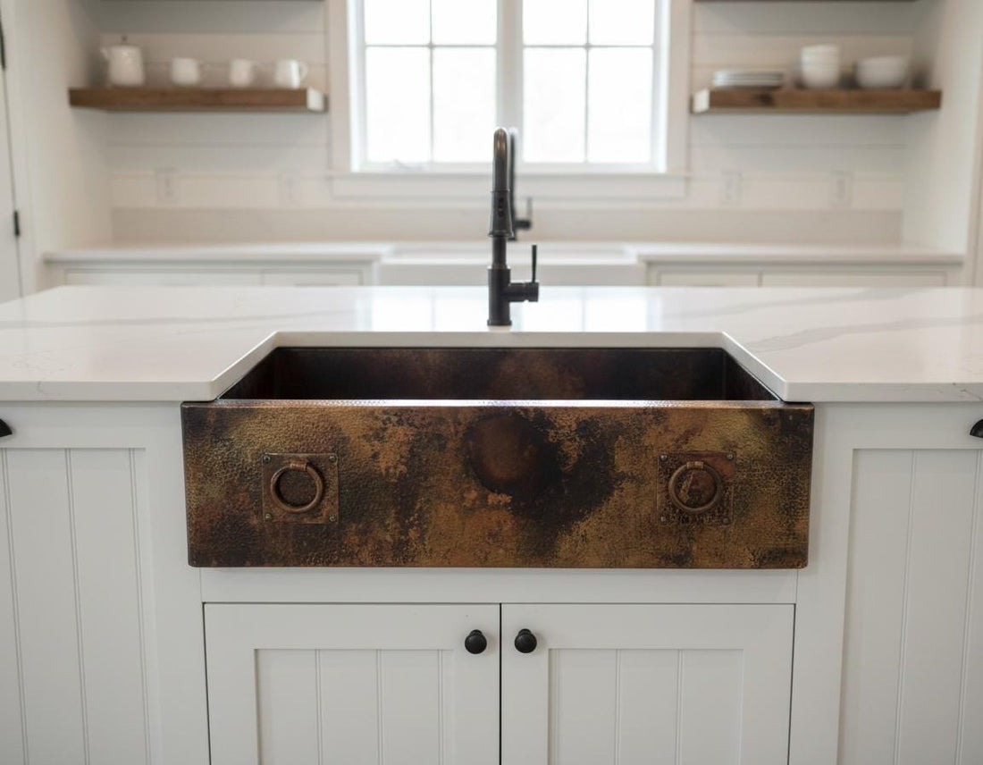Bronze farmhouse sink in a kitchen with white cabinets and marble countertop.