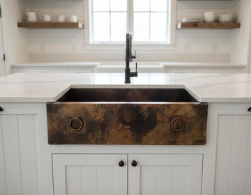Bronze farmhouse sink in a kitchen with white cabinets and marble countertop.
