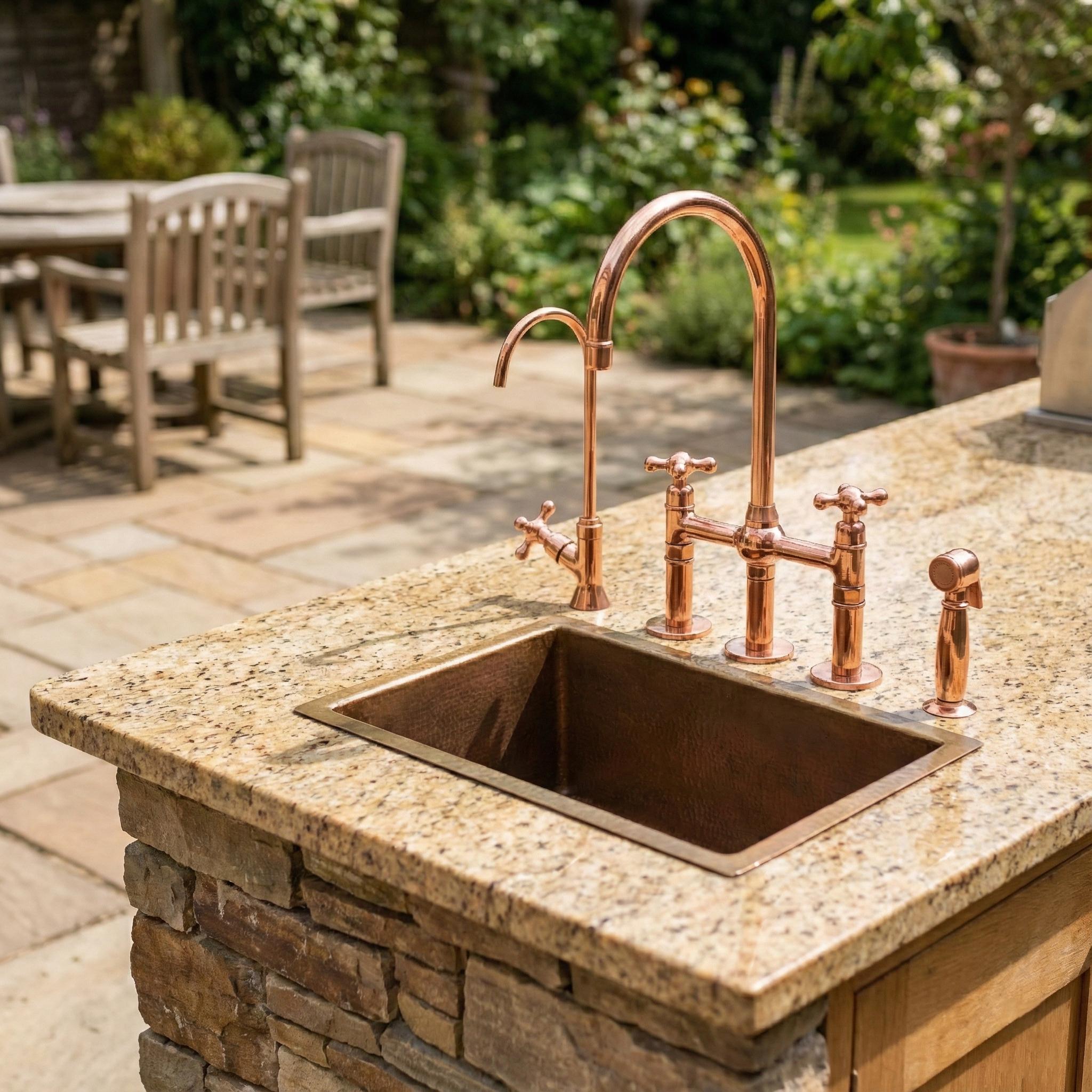 Outdoor kitchen sink with copper faucet and fixtures on a stone countertop.