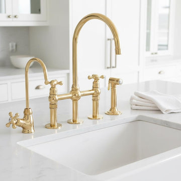Gold kitchen faucet set on a white countertop with a blurred background