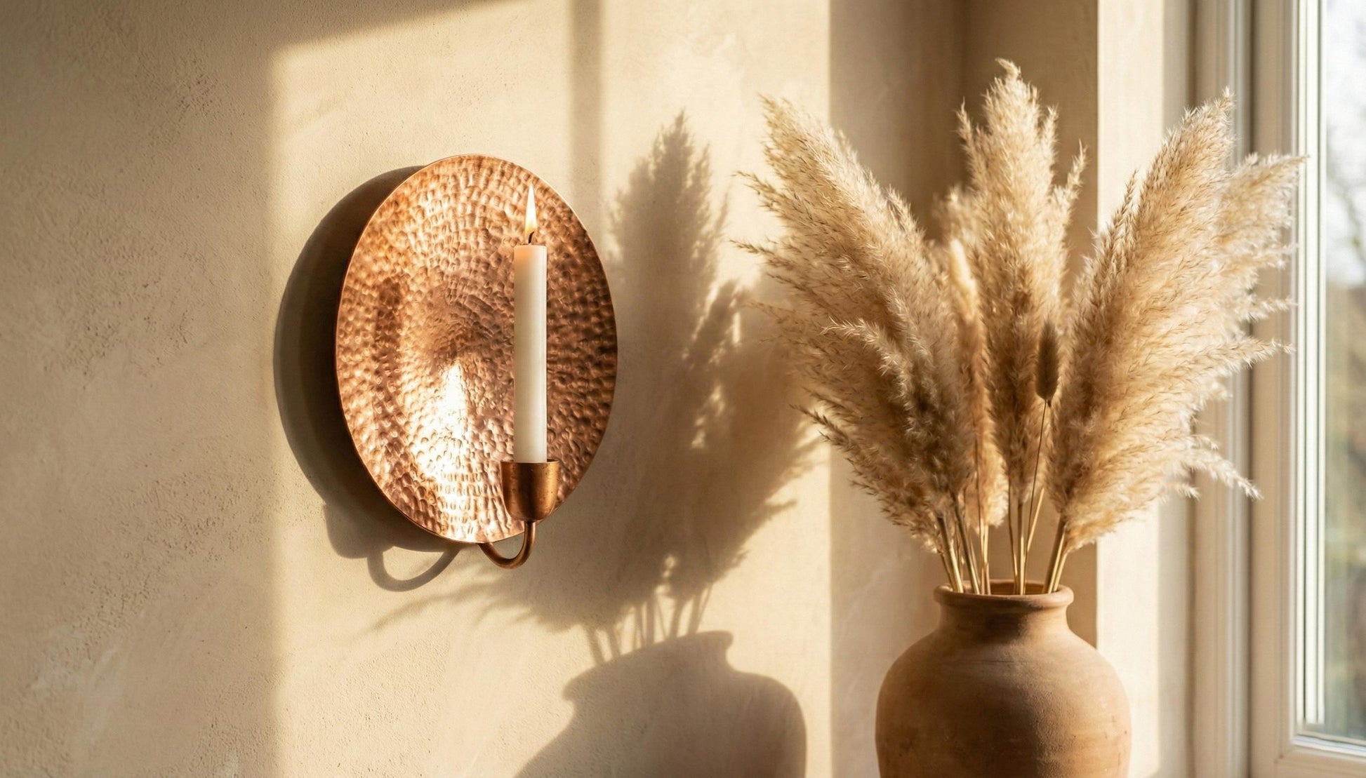 Copper wall sconce with a candle and a vase of dried pampas grass on a neutral wall.