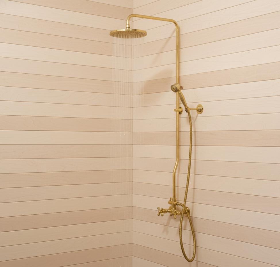 Gold shower head and control panel against a beige tiled wall