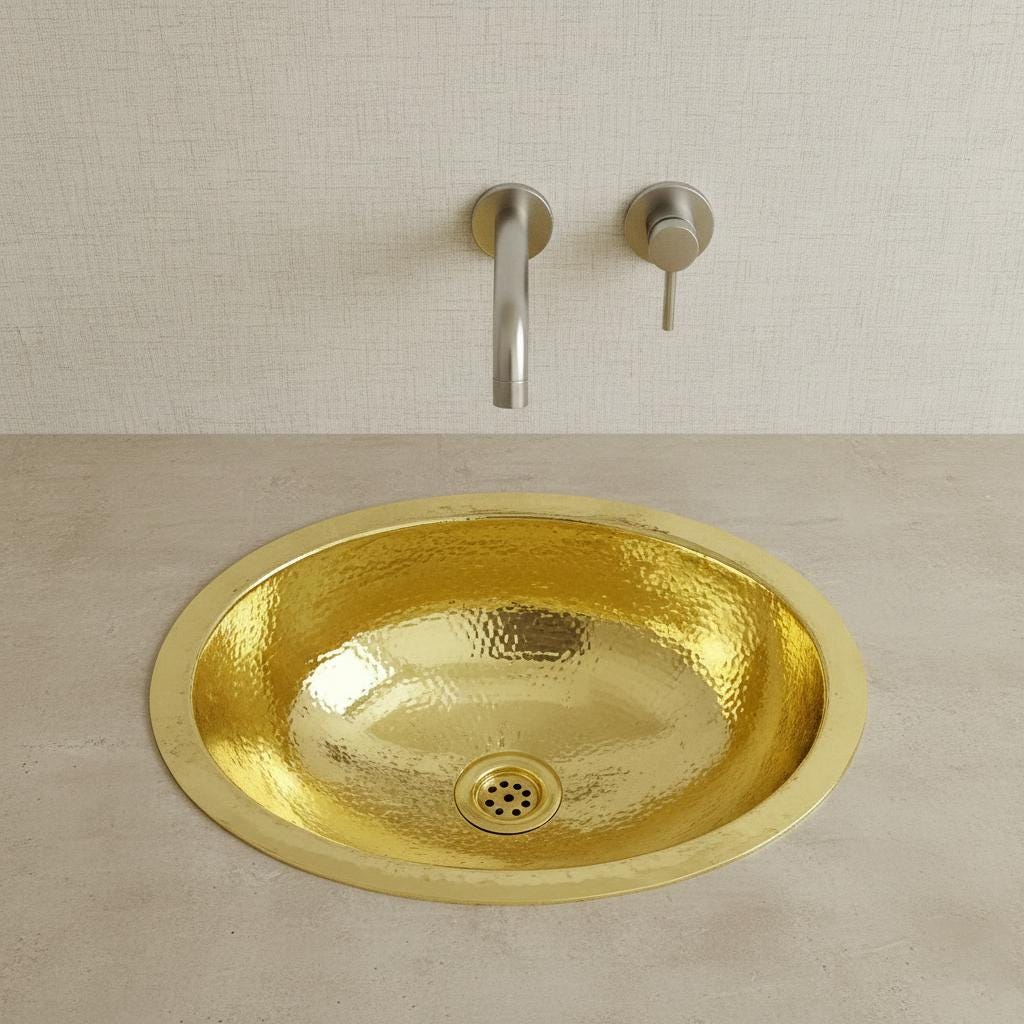 Gold sink with silver faucet on a beige countertop against a light wall.