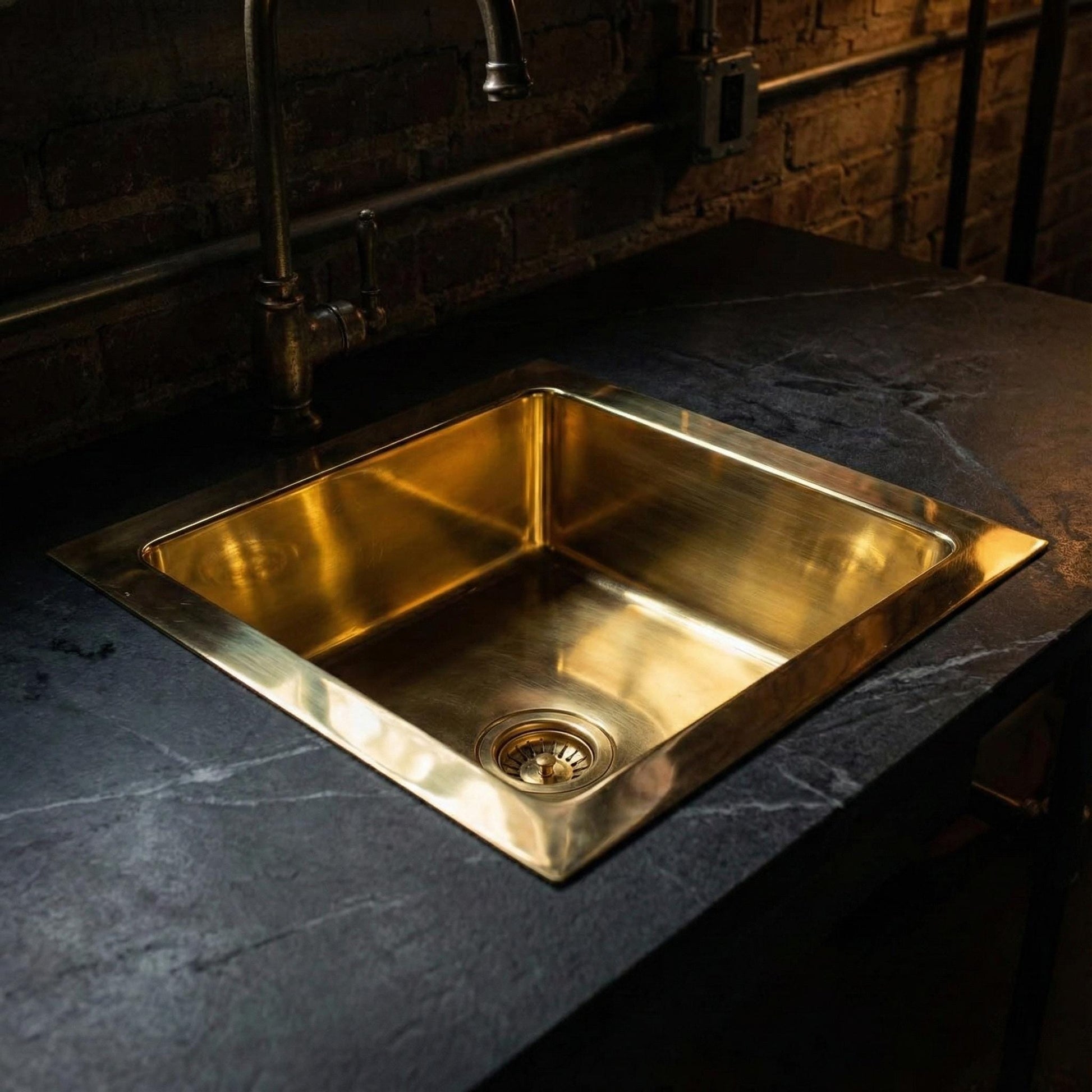 Gold sink on a dark countertop with a rustic wall background
