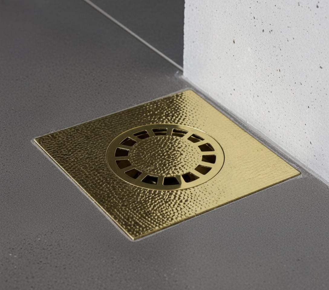 Gold square drain cover on a gray floor with white wall