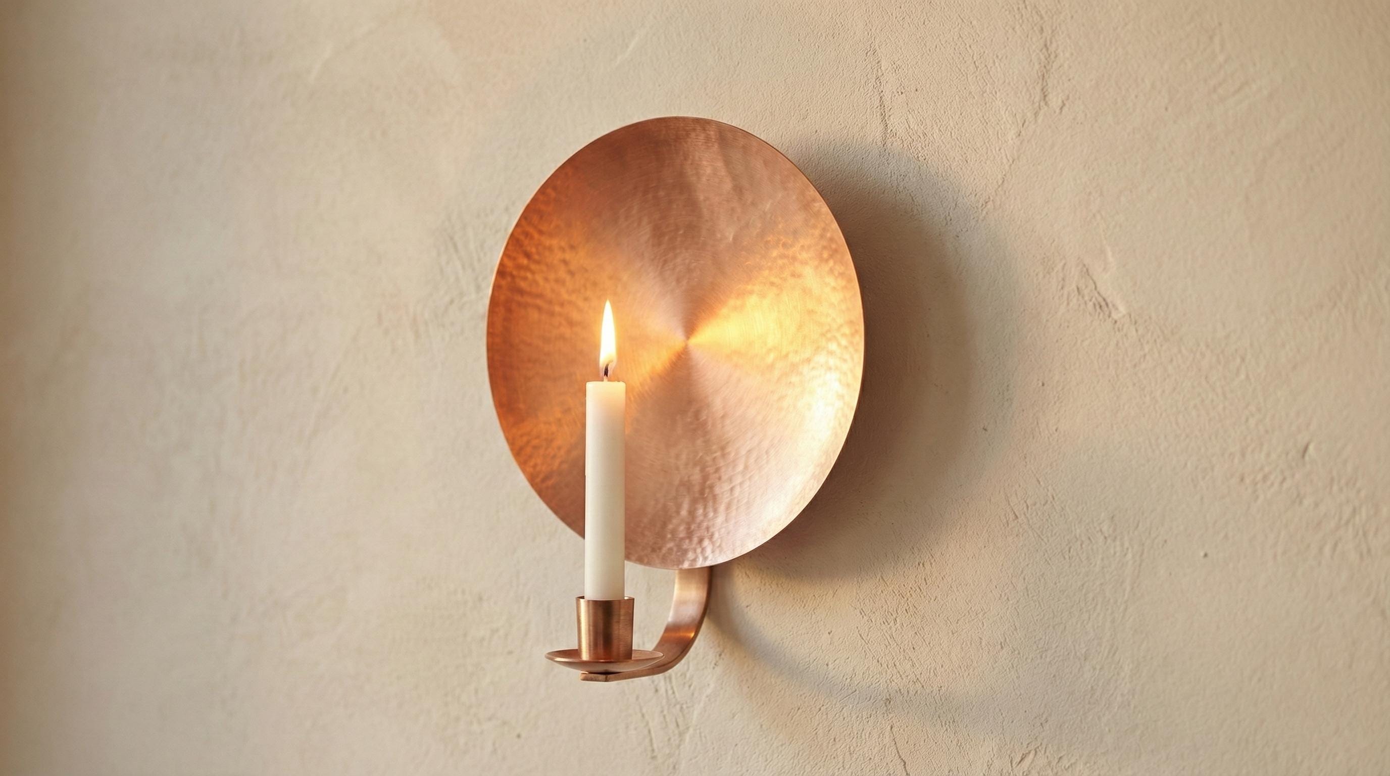 Copper wall sconce with a lit candle on a beige wall