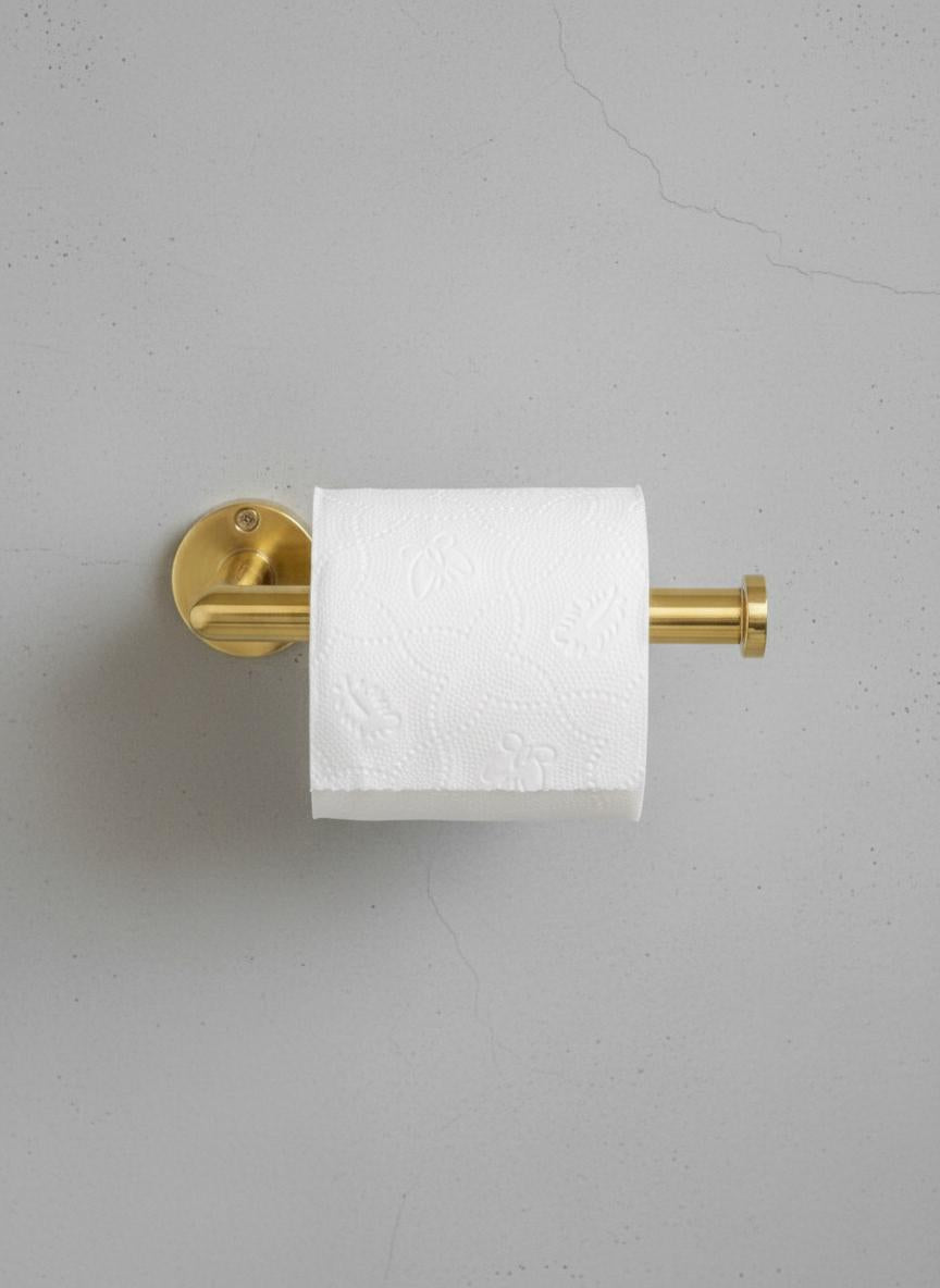 Gold toilet paper holder with a roll of toilet paper on a gray wall