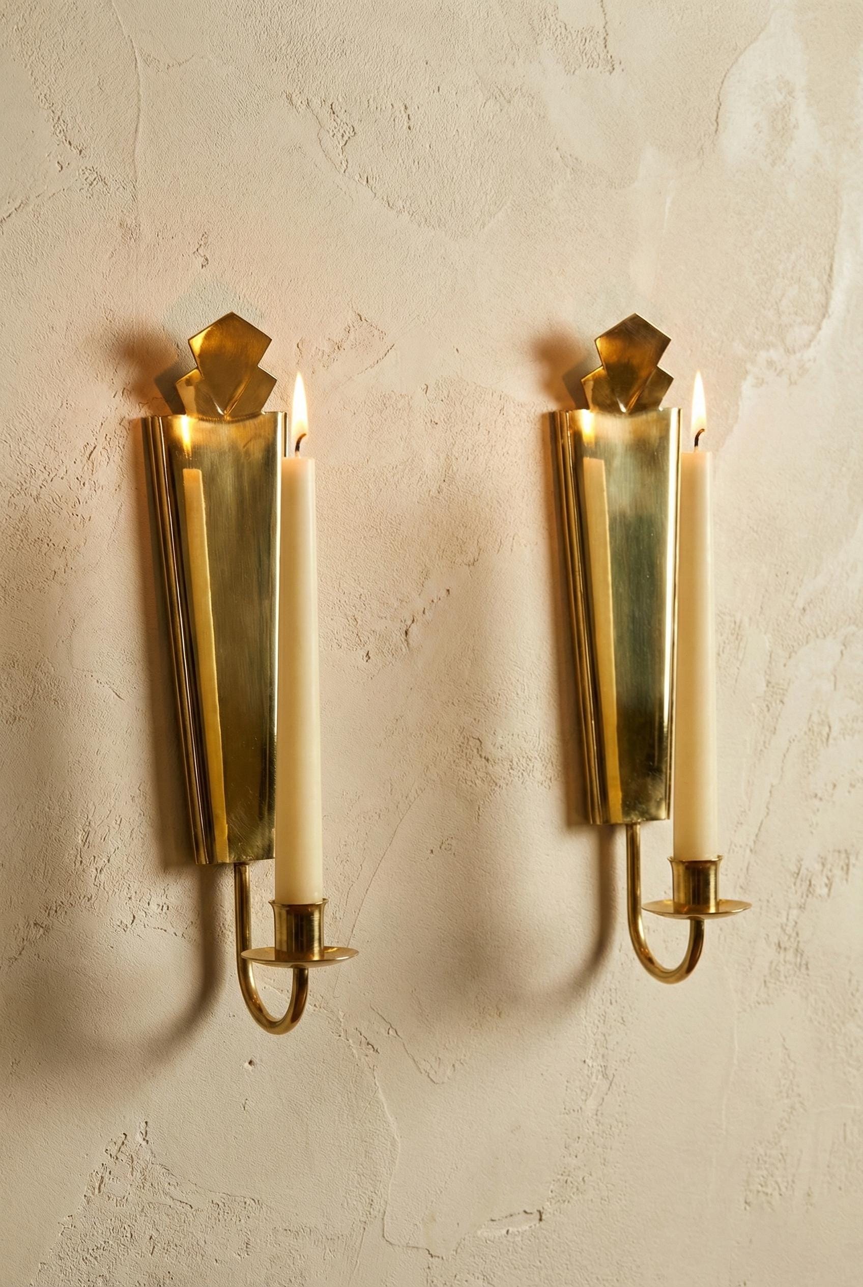 Two brass wall sconces with candles on a textured beige wall.