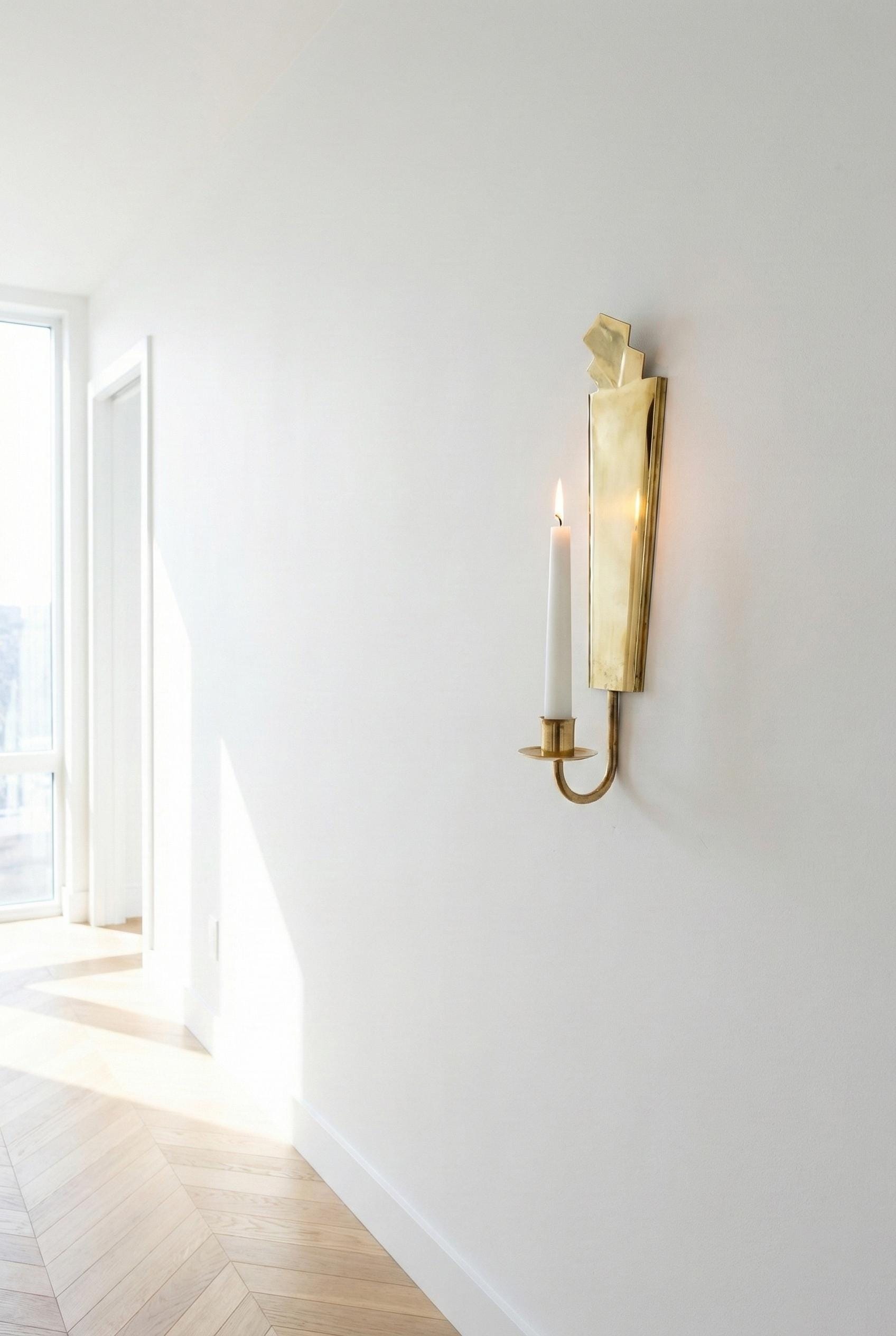 Gold wall sconce with a candle on a white wall in a bright room.