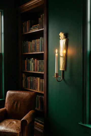 Bookshelf against a dark green wall with a lit candle and sconce.