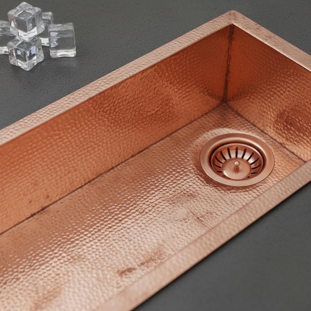 Copper kitchen sink with a textured finish on a dark surface.