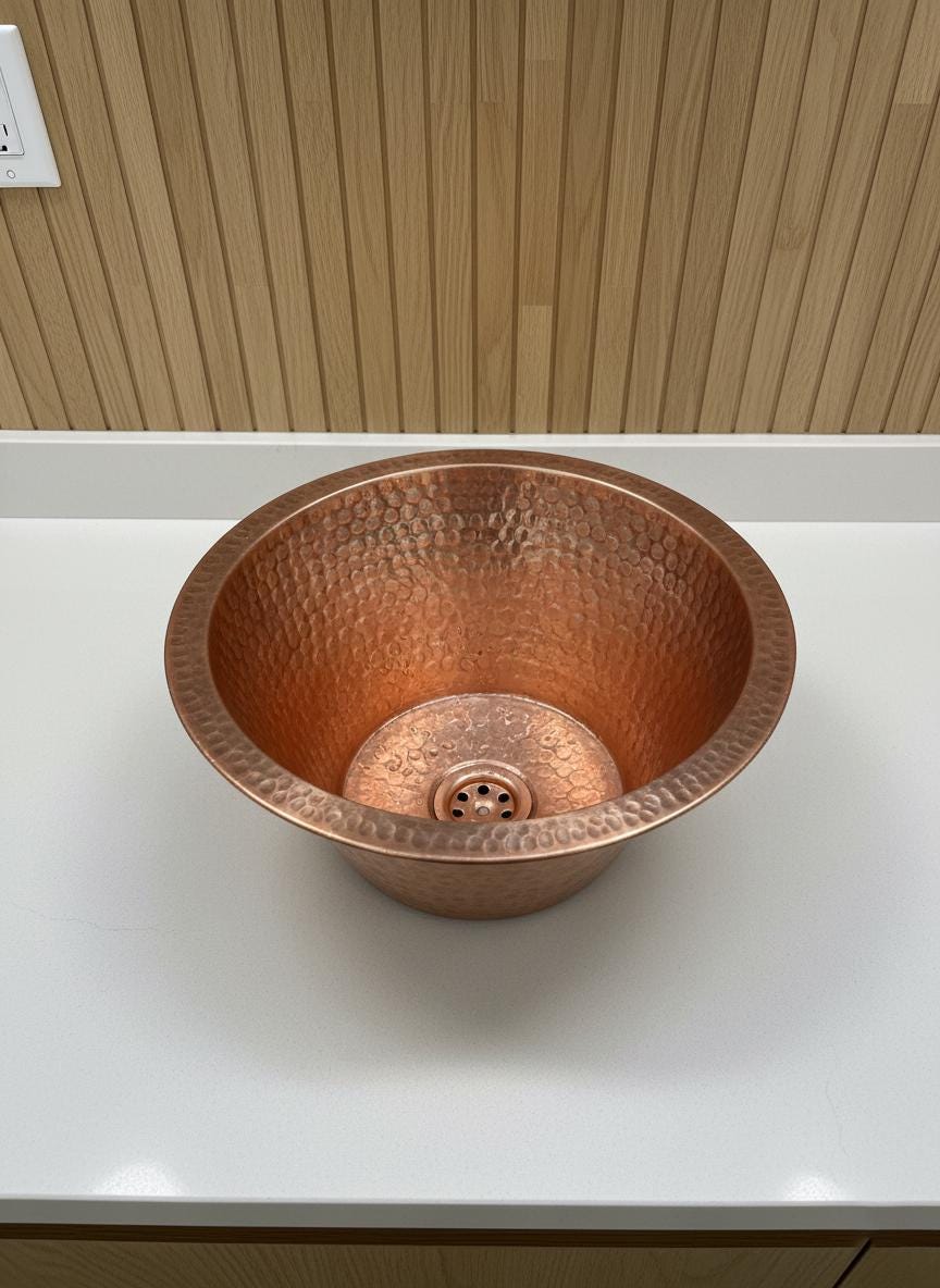 Copper sink on a white countertop with wooden wall background