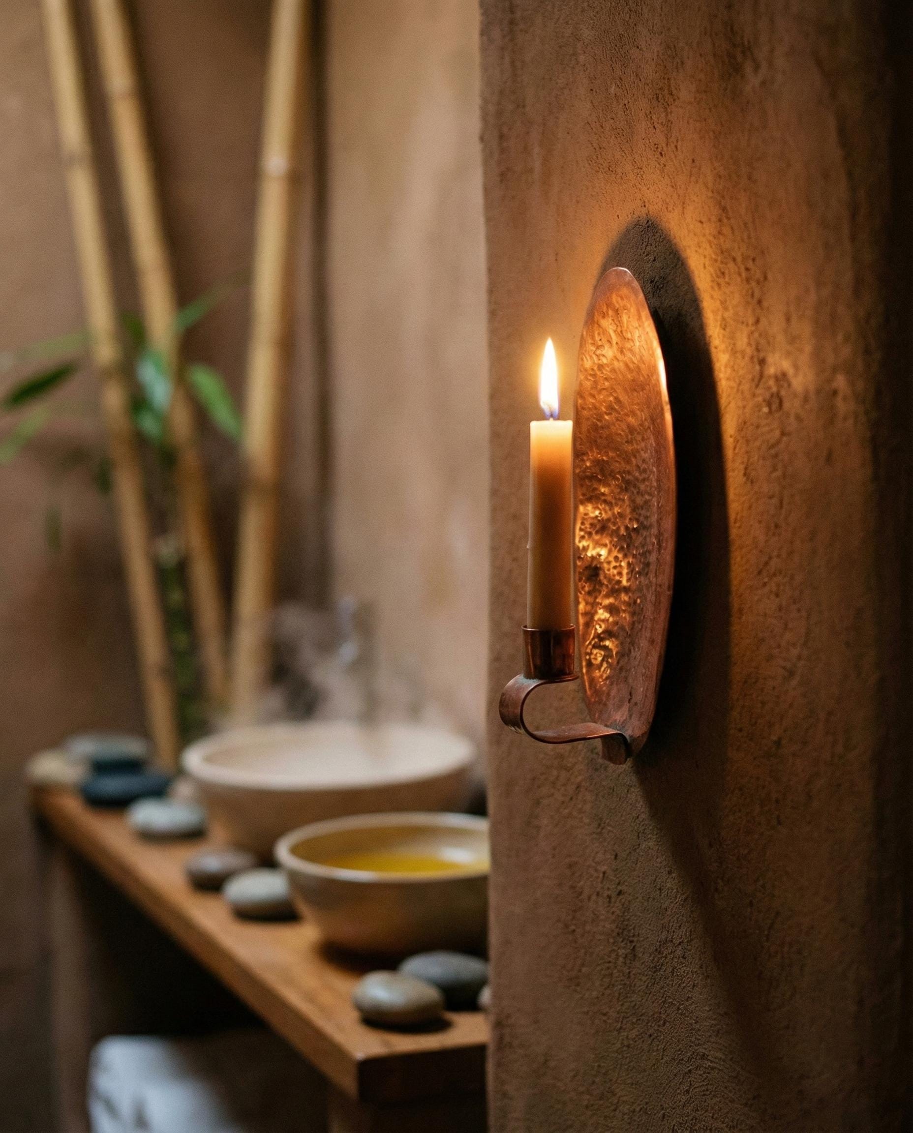 Candle in a wall-mounted holder with a serene setting featuring a bowl, stones, and bamboo.