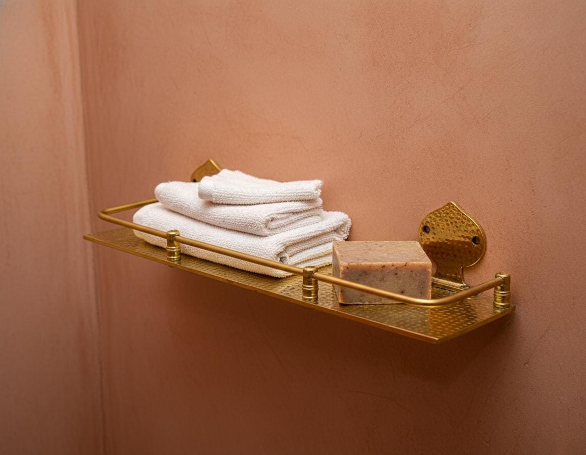 Gold towel rack with folded towels and a bar of soap on a peach-colored wall.