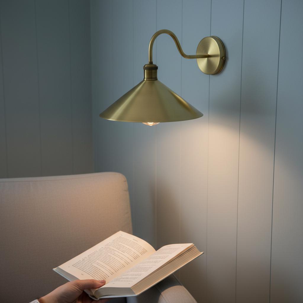 Person reading a book under a wall-mounted brass lamp in a cozy room.