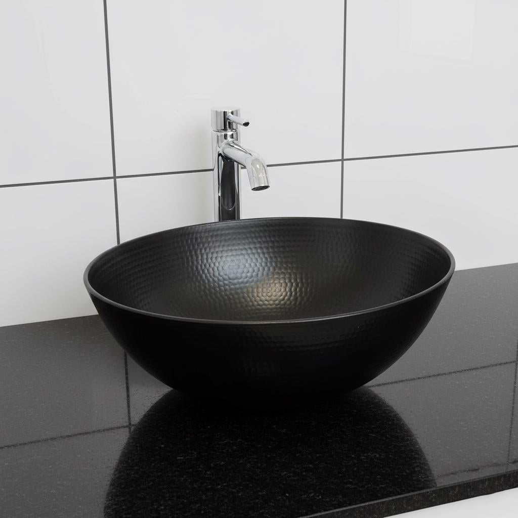 Black round sink with silver faucet against a tiled bathroom wall.